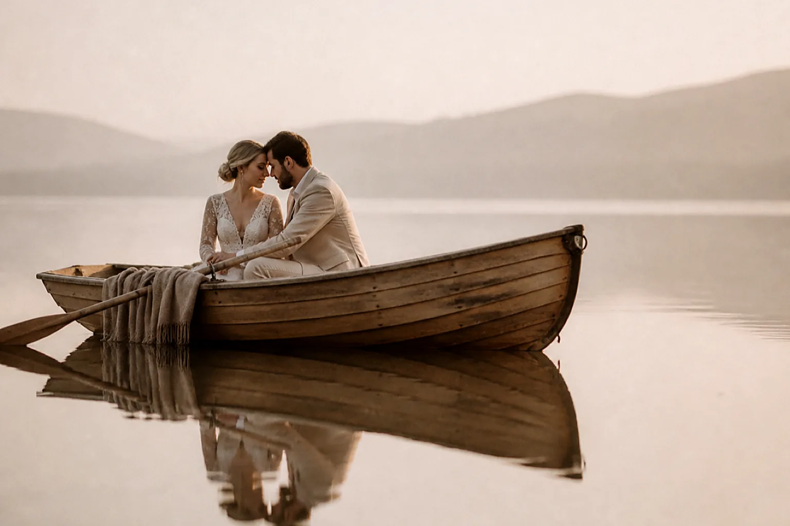 A couple in a small wooden rowing boat on a perfectly still lake at dawn