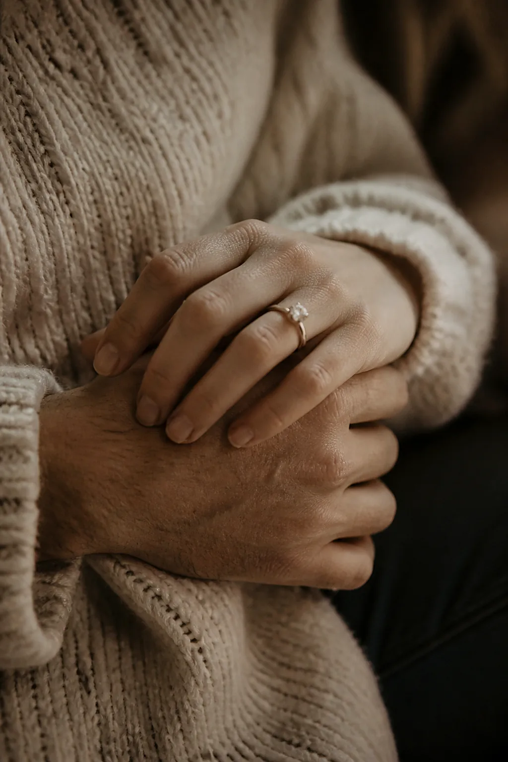 A couple's interlaced hands on a cream wool sweater with an engagement ring